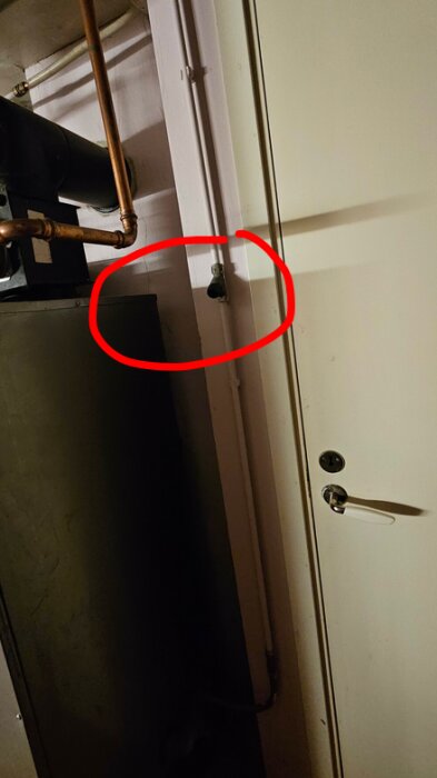 Påfyllningsventil i ett rum med rör och dörr, markerad med röd cirkel.