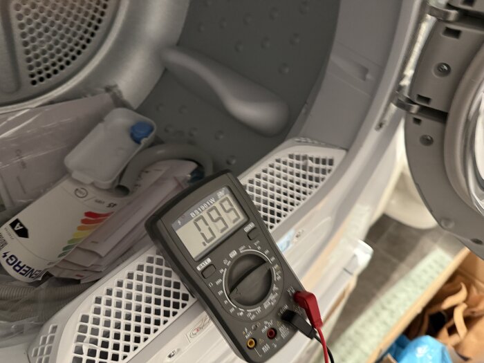 Multimeter avläser resistans på 0,095 kOhm placerad inuti en maskin, möjligtvis en torktumlare.