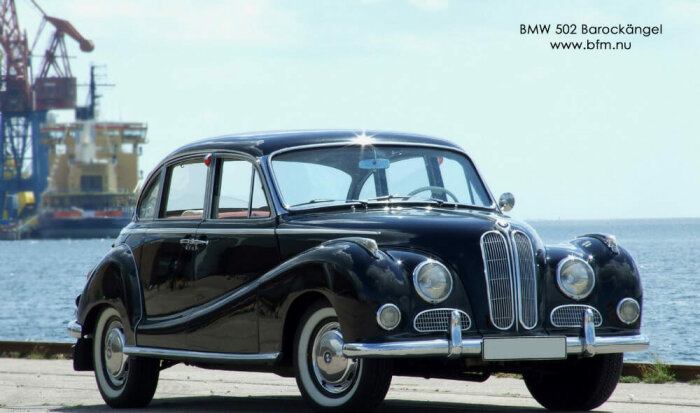 Svart BMW 502 Barockängel parkerad vid vattnet med industrikranar i bakgrunden.