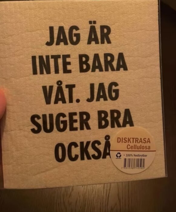 En beige disktrasa av cellulosa med texten "JAG ÄR INTE BARA VÅT. JAG SUGER BRA OCKSÅ" samt etikett "100% Nedbrytbar".