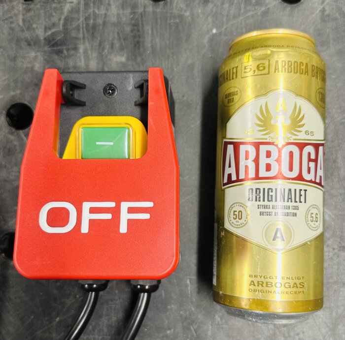 Röd brytare märkt "OFF" bredvid en guldfärgad Arboga ölkanna.