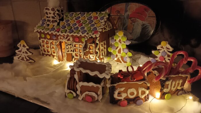 Pepparkakshus i form av stationshus med vägghängd klocka, dekorerat med godis och glasyr, framför ett ankommande pepparkakståg.