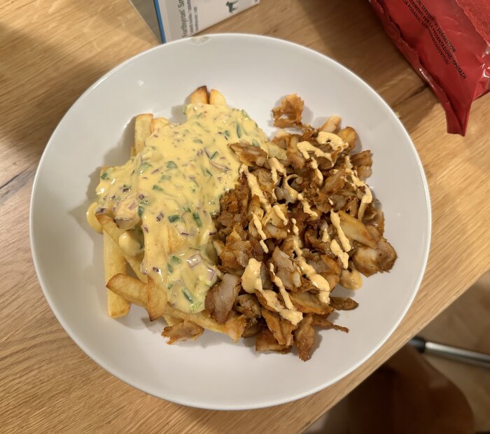 Tallrik med pommes frites täckta med smältost och serverade med kebabkött och sås på ett träbord.