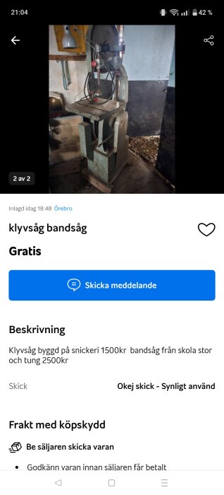 Bild på en klyvsåg eller bandsåg i ett verkstadsutrymme, med sladdar som hänger och sågblad synligt. Maskinen ser använd ut.