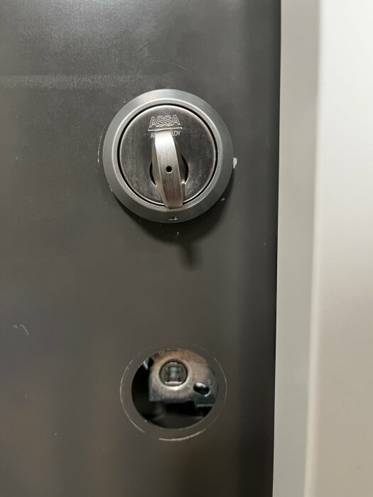 Närbild på ett delvis demonterat dörrlås med synligt vred och dekorhylsa från märket ASSA, samt en öppning där en spärr syns.