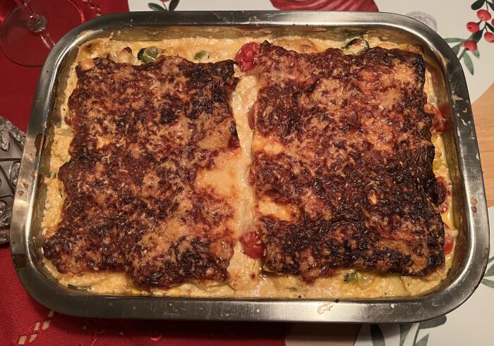 Skaldjurslasagne med ricotta och tomat i ugnsform, serverad på röd bordsduk, dekorerad med blad på underlägget.