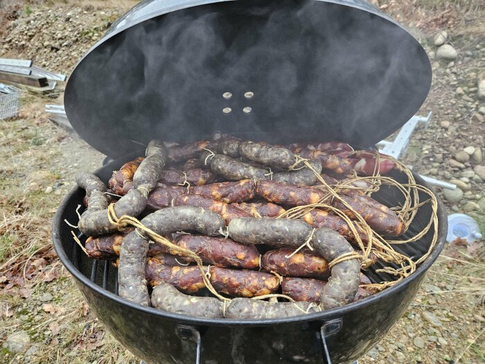 Rök fylld med hantverkskorvar på en grill under utomhusredna dag.