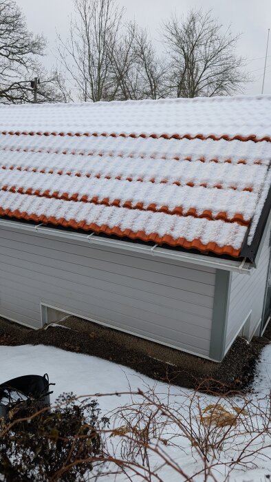 Garage med snötäckt tak; synliga takpannor under snön och blottade träreglar diskuteras som problem vid regn och snö.