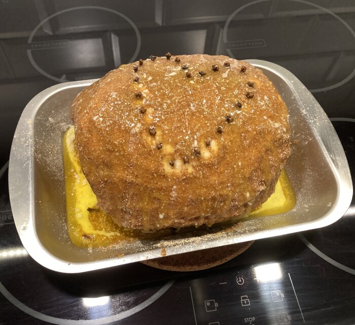 Julskinka färdiggriljerad i ugnsform, toppad med kryddnejlikor och smör, klart för servering.