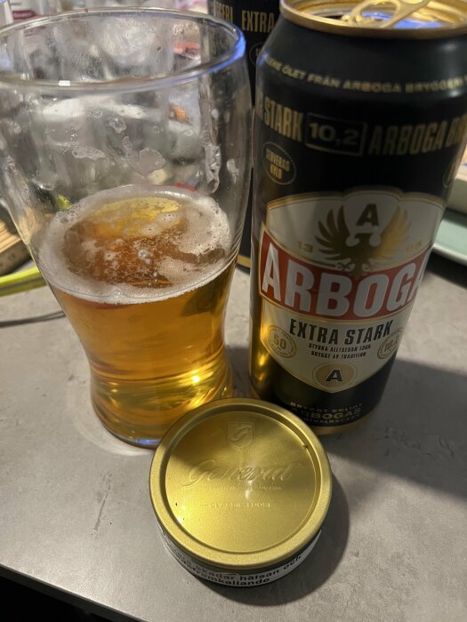 Ölglas med Arbogas starköl, en snusdosa av märket General på ett bord.