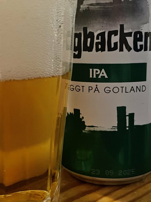 En grön och vit ölburk märkt "IPA" bredvid ett glas öl med skum.