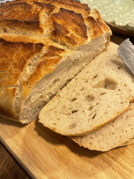 Nygräddat bröd på en skärbräda, delvis skivat med en kniv, visar krispig skorpa och luftig inkråm.