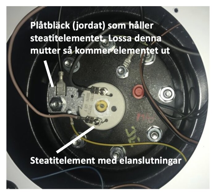 Närbild av steatitelement med elanslutningar och jordad plåtbleck med instruktioner för att lossa mutter.