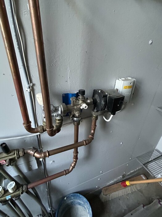 Rörsystem och ventiler i en värmepumpsinstallation mot en vägg, med kopparrör och anslutningar för golvvärme i ett hus.