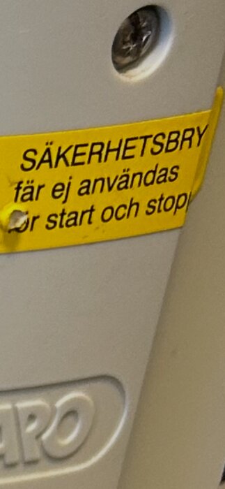 Gul skylt med texten "SÄKERHETSBRYTARE får ej användas för start och stopp" på en maskin eller apparat.