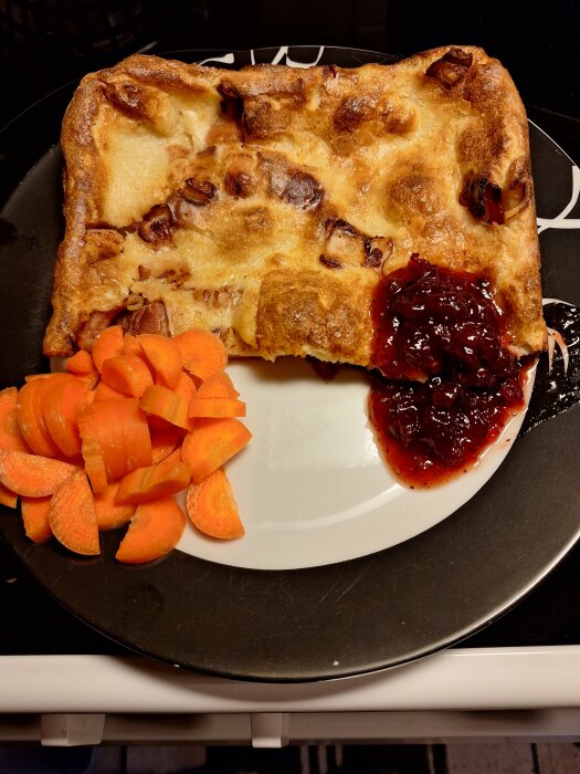 Ugnspannkaka med bacon, lingonsylt och skivade morötter på en svartvit tallrik.