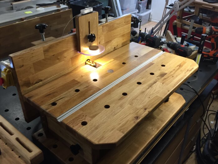 En horisontalfräs i träverkstad, belyst av en lampa, med verktyg och borrmaskiner i bakgrunden.