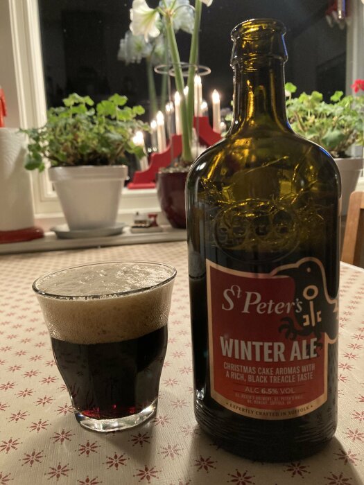 Flaska och glas med St. Peter's Winter Ale på ett juldekorerat bord, med levande ljus och växter i bakgrunden.