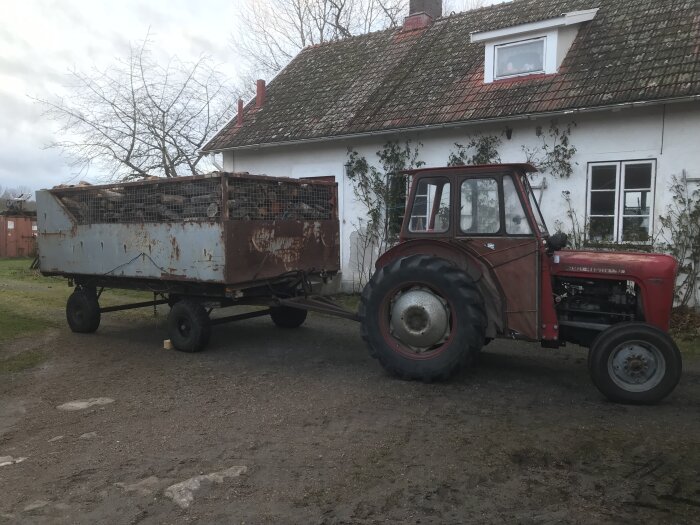 Röd MF-35 traktor framför vit byggnad, drar släpkärra med 10 kubikmeter blandved.