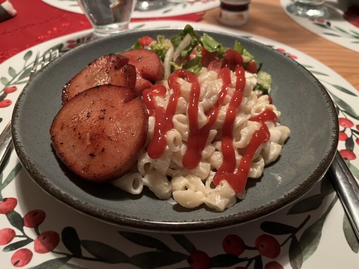 Tallrik med mjölkstuvade makaroner, stekt falukorv, sallad och ketchup på ett julmönstrat bord.