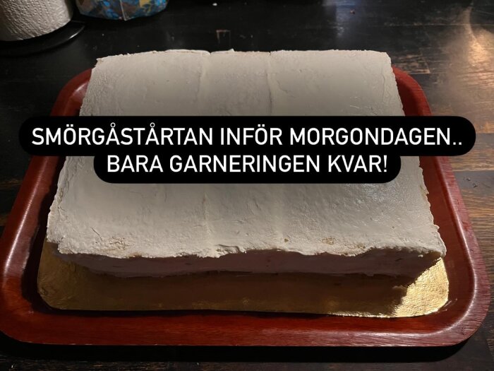 En rektangulär smörgåstårta på ett rött fat, redo för garnering. Texten "Smörgåstårtan inför morgondagen, bara garneringen kvar!" över bilden.