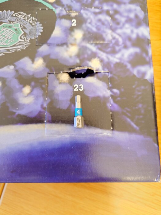 Adventskalender med en öppnad lucka nummer 23, som avslöjar ett bits på en blå bakgrund.