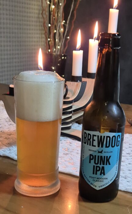 Ölglas med skummande Brewdog Punk IPA bredvid en adventsljusstake med tända ljus på ett bord.