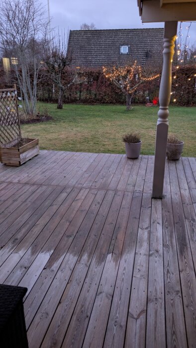 Trädäck med julbelysning i träden, ingen snö på marken, en mulen himmel syns från verandan under jul.