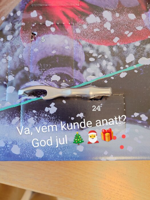 Adventskalender med luckor och texten "Va, vem kunde anat? God jul" samt emojis; nyckelring med öppnare ligger ovanpå.