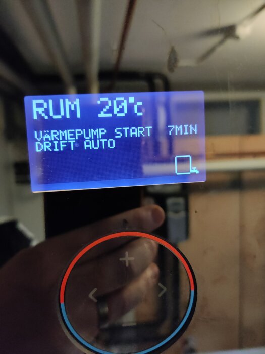 Displayen på en bergvärmepump visar rumstemperatur 20°C, värmepumpstart om 7 minuter och driftläge auto, med temperaturreglage under.