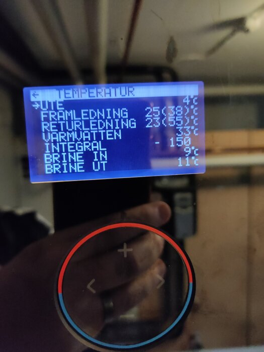 Närbild på bergvärmepumpens display med temperaturer: utomhus, framledning, returledning och varmvattnet, samt en kontrollknapp med rödblå markering.