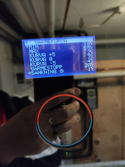Närbild av en display till bergvärmepump som visar temperaturinställningar som "Värmekurva" med olika kurvor och "Sänkning". Reflektion av en hand syns.
