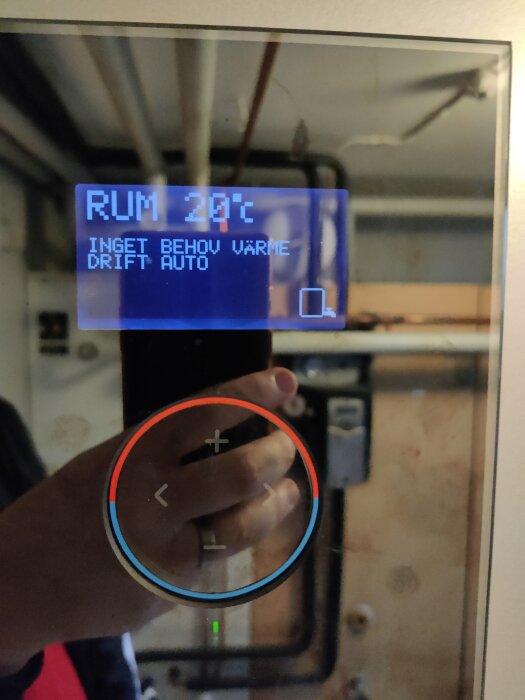 Display på bergvärmepump visar 20°C och meddelanden om inget värmebehov samt automatiskt läge. Röd och blå ring med pilar syns också på skärmen.