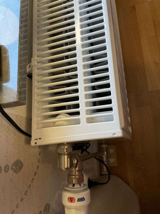 Radiator under ett fönster med ventil och röranslutningar, en av radiatorerna är dubelt så tjock som de andra.