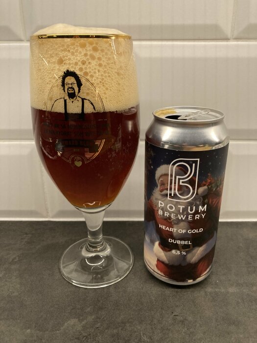 Ett glas fyllt med brun öl med rik skumkrona bredvid en ölbok från Potum Brewery med julmotiv.