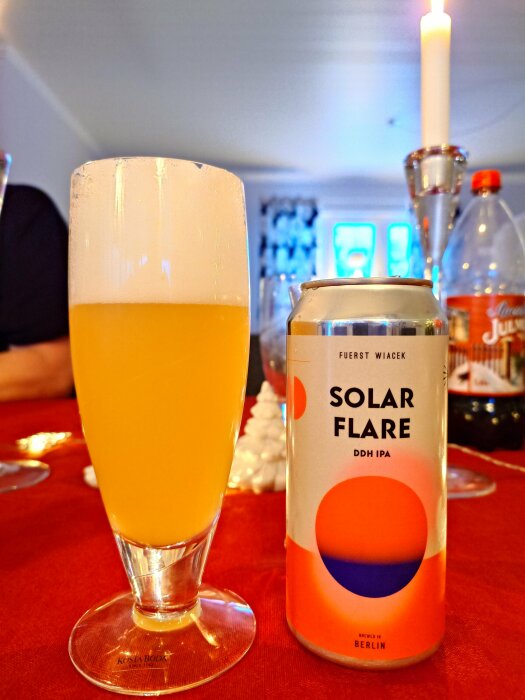 Glas med öl och en Solar Flare DDH IPA burk på ett dukat bord med tända ljus i bakgrunden.