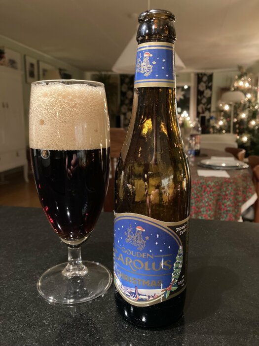 Glas och flaska av Gouden Carolus Christmas-öl på ett bord, med en julgran i bakgrunden.