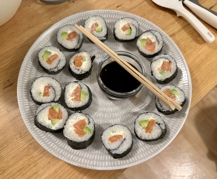 Sushi med lax och avokado på tallrik, pinnar och soyaskål.