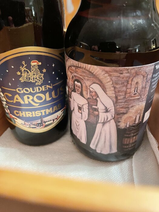 Två julölsflaskor, en med etikett "Gouden Carolus Christmas" och den andra med etikett föreställande två munkar i kloster.