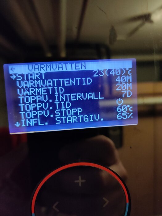 Bild på en digital termostatdisplay som visar varmvatteninställningar med temperaturer och tidsuppgifter, omgiven av en kontrollpanel.