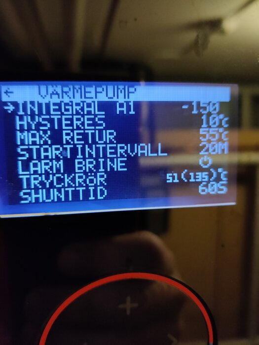 Display för värmepump visar inställningar som max retur och startintervall tillsammans med siffror och en röd styrknapp nederst.