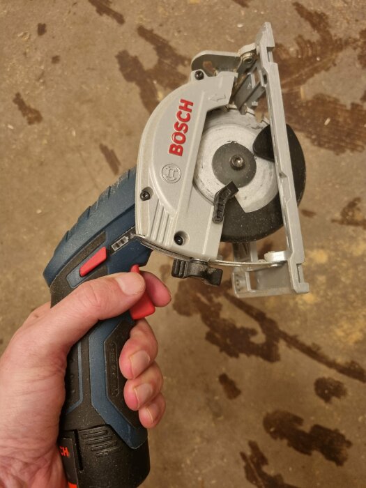 Hand håller en Bosch cirkelsåg, använd för att såga 60x60 cm rutor i gammalt golv.
