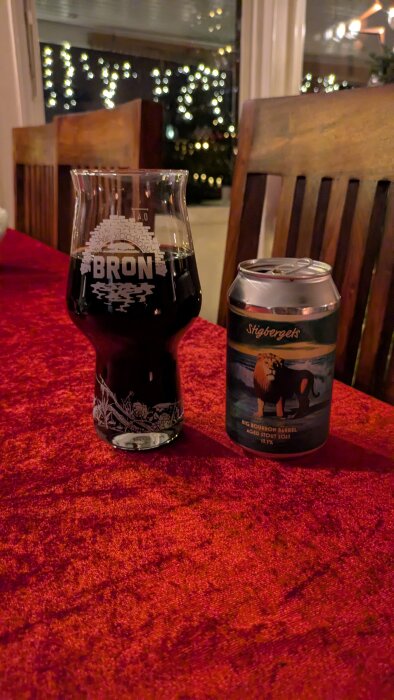 Ett glas och en burk med mörk stoutöl, märkt Stigbergets Big Bourbon Barrel Aged Stout 2023, på ett bord med röd duk.