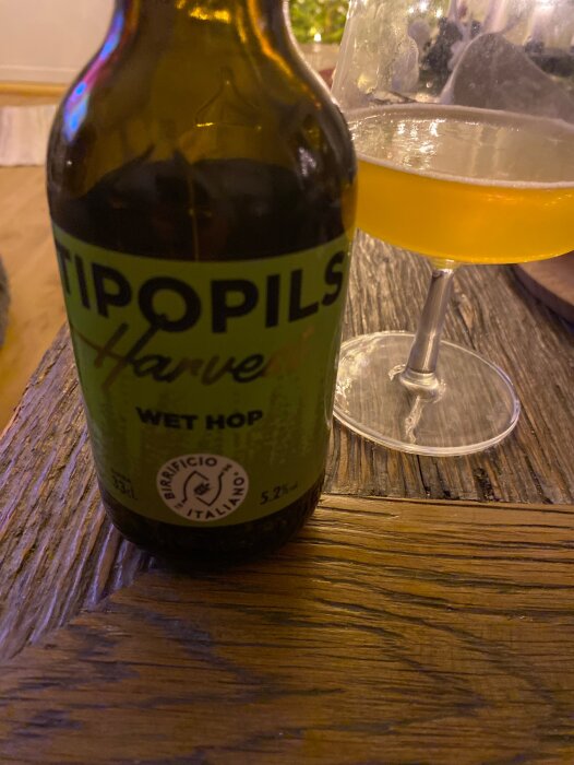 Flaska och glas med italiensk pilsner Tipopils med etikett "Wet Hop" och text om smaknoter bredvid ett glas med gyllene dryck på träbord.
