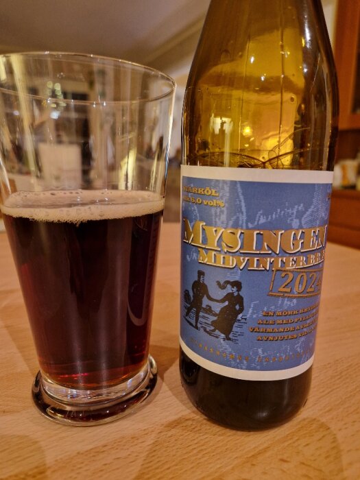 Flaska och glas med Mysingen midvinterbrygd från Nynäshamns Ångbryggeri på ett träbord.