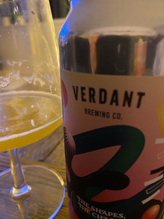 Burk med Verdant Brewing Co. öl och ett halvtomt glas med IPA på ett bord.