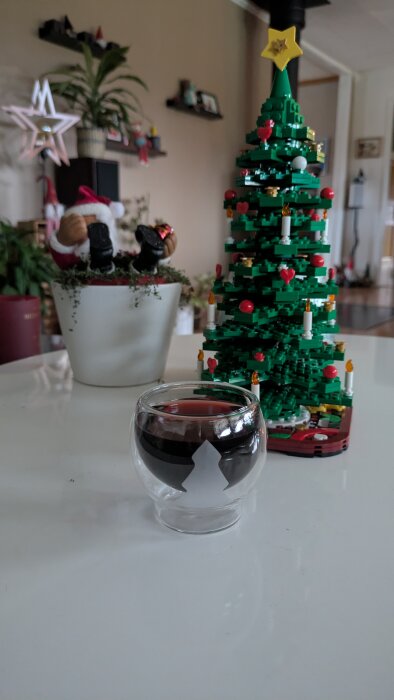 Ett glas med glögg på ett bord, bredvid en LEGO-julgran och en blomkruka med en tomtefigur.