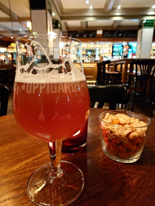 Ett glas Oppigårds Ramsen öl på ett bord i en bar, bredvid en skål med snacks och ett rött värmeljus.