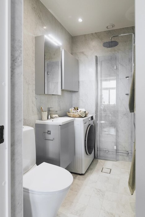 Modernt badrum med dusch, tvättmaskin och handfat, designat av en hantverkarfirma specialiserad på våtrum i Stockholm.