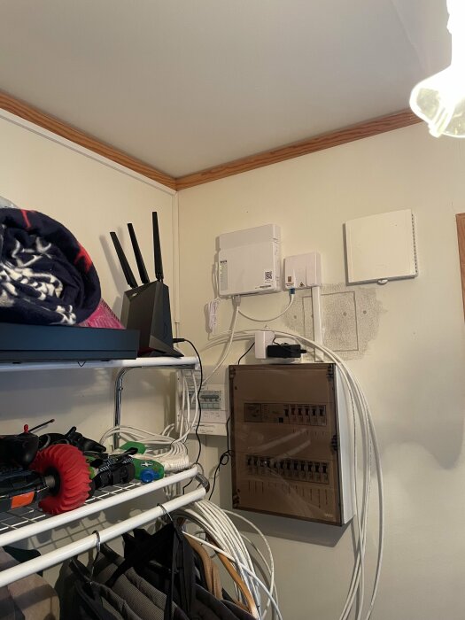 Elektrisk panel och router i ett rum med kablar och verktyg på en hylla; utmanande installation.